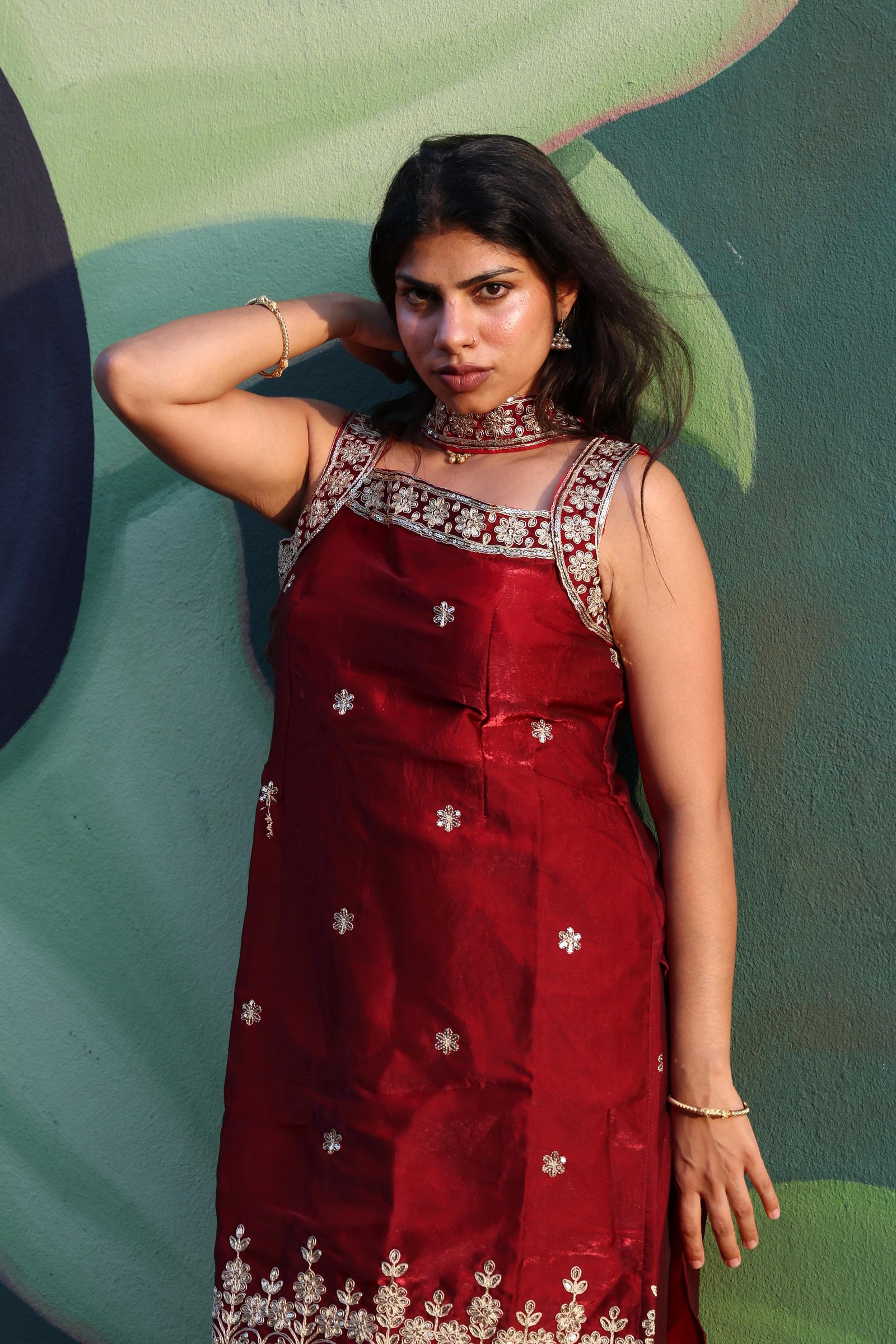Vandana wearing deep red Indian fashion against a graphic mural
